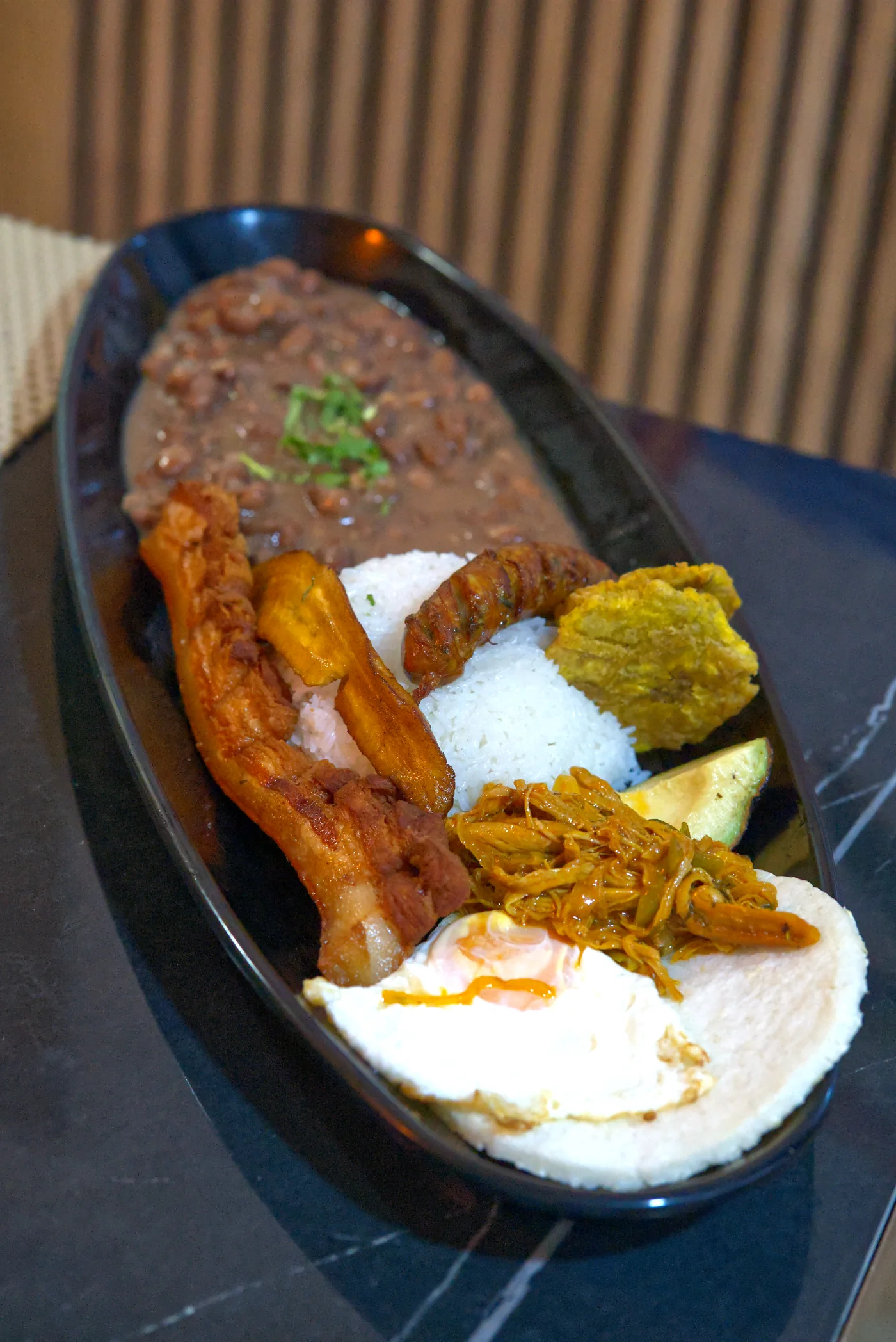 Bandeja Caribe con frijoles, arroz, chicharrón, chorizo, carne desmechada, huevo y plátano